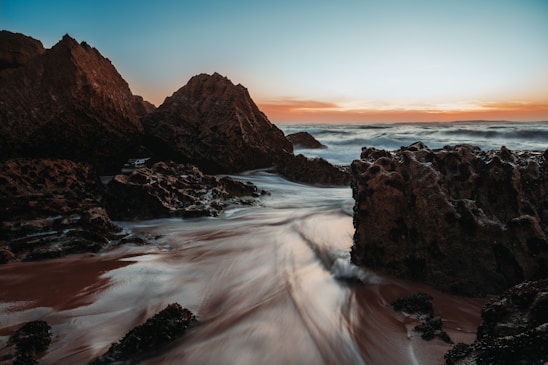 A serene coastal scene with waves gently crashing against rocky shores under a soft sunset.