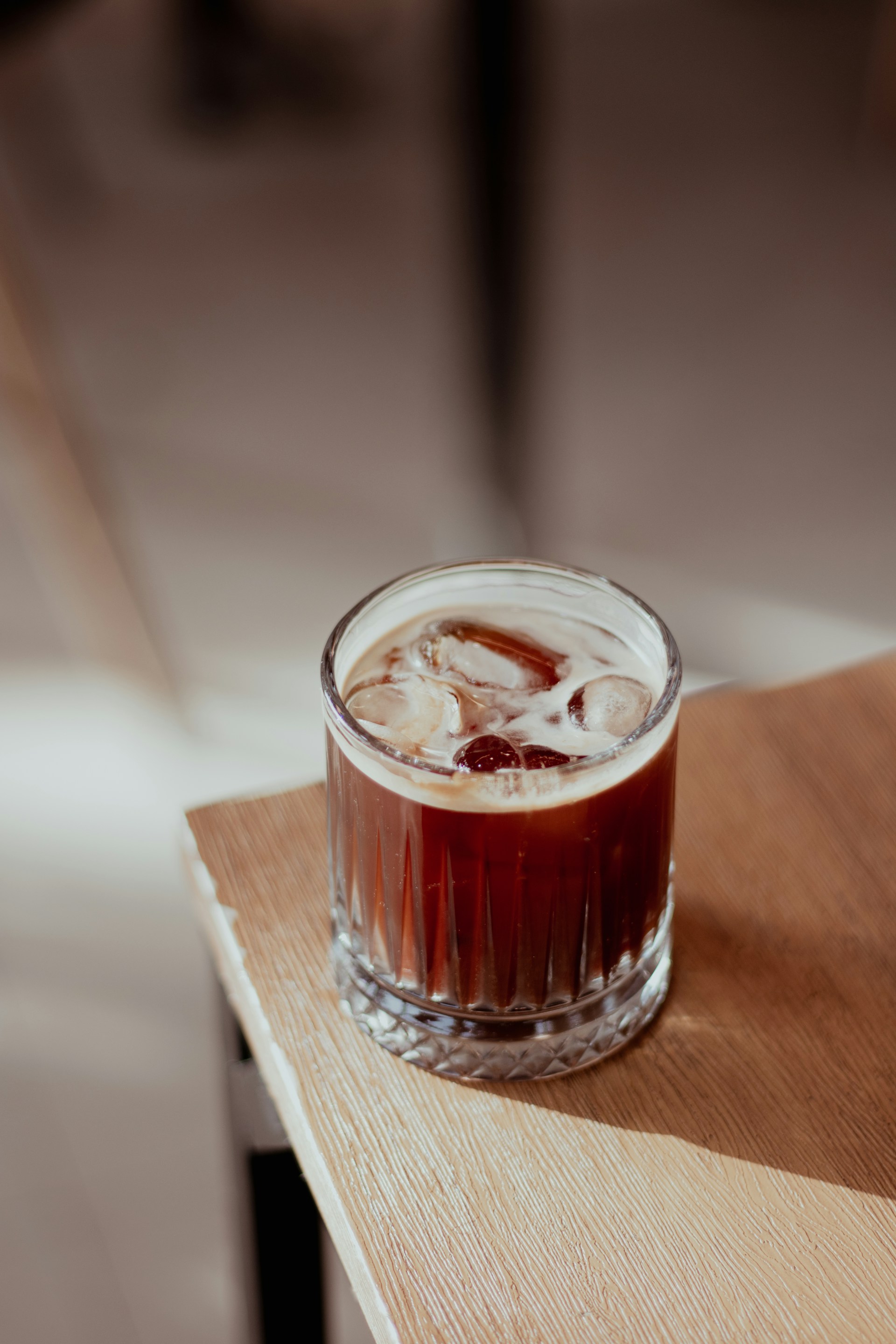 An inviting glass of iced kopi with condensation, placed on a wooden table with a blue backdrop.