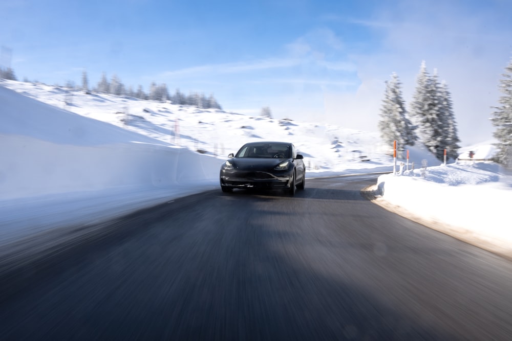 a black car driving down a snow covered road