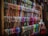 A display of numerous colorful scarves is organized neatly on wooden shelves. The scarves are arranged in rows, showcasing a variety of patterns and fabrics. A mannequin dressed in a sleeveless dress is positioned to the right side of the image.