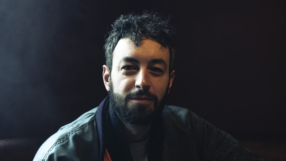 a man with a beard sitting in a dark room