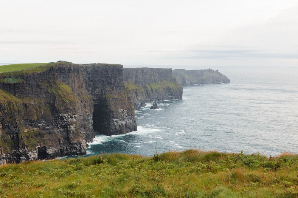 a grassy field next to a cliff with a body of water