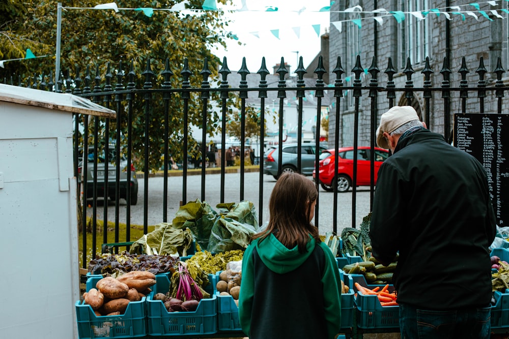 a man and a little girl standing in front of a fruit and vegetable stand