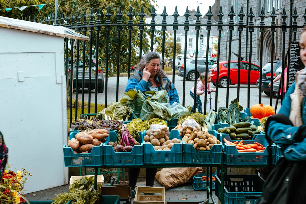 a woman talking on a cell phone next to a table full of vegetables