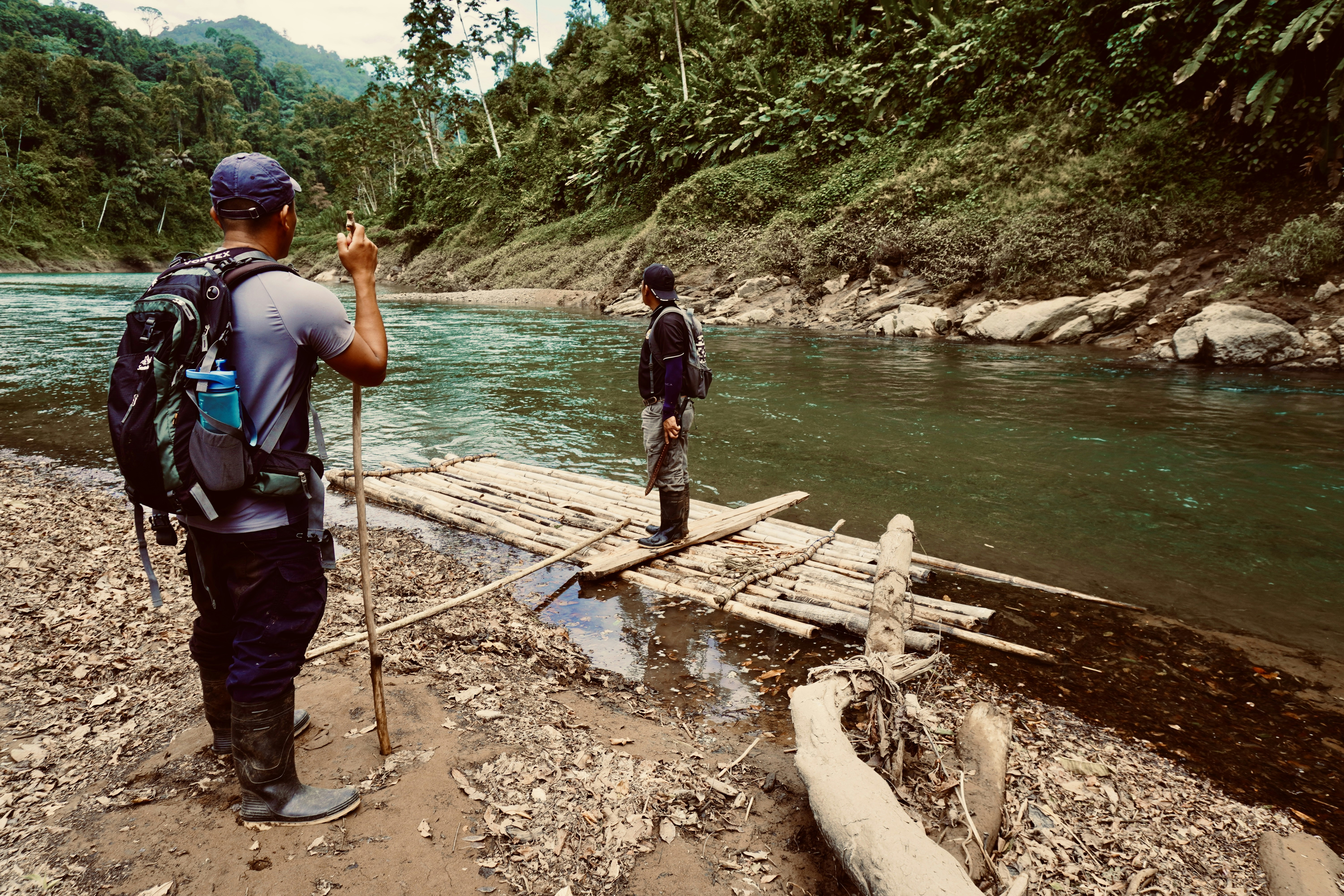 a man standing on a wooden raft next to a river