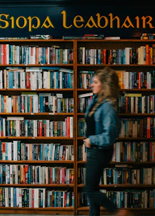 a woman walking past a book shelf filled with books