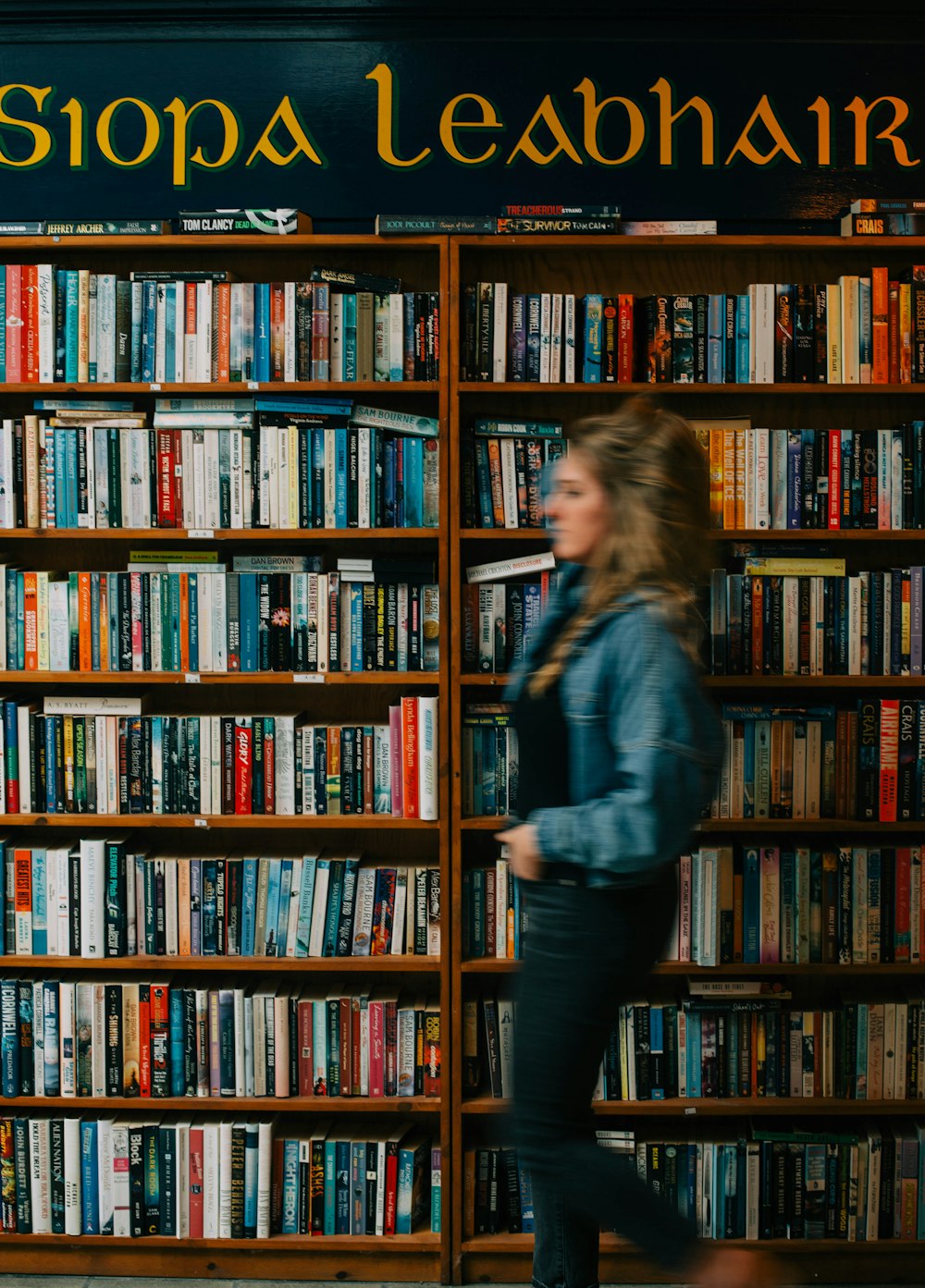 a woman walking past a book shelf filled with books