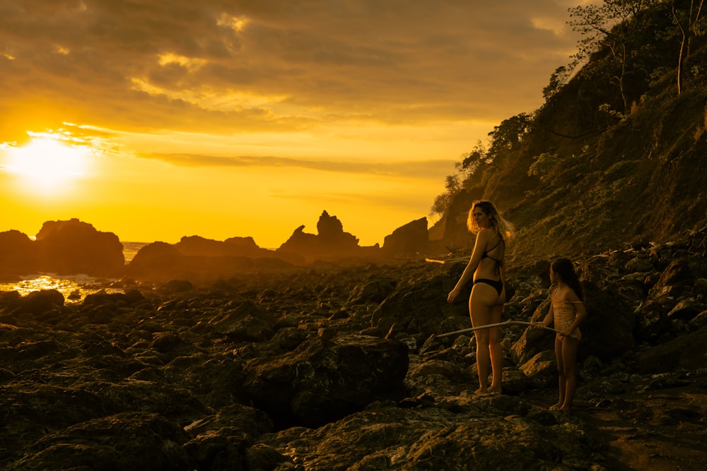 a couple of women standing on top of a rocky beach