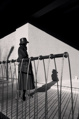 a man in a trench coat and hat standing on a fence