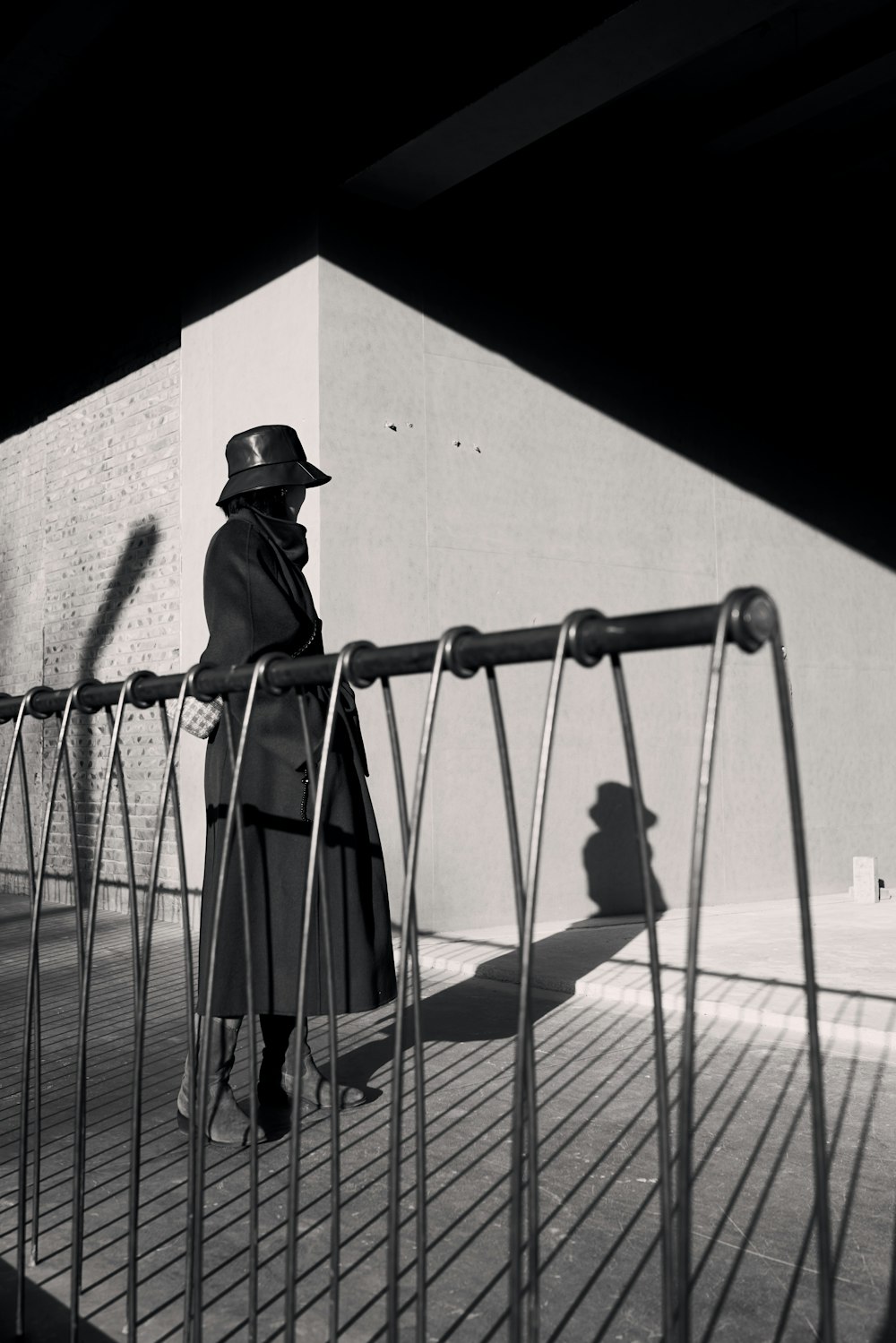 a man in a trench coat and hat standing on a fence