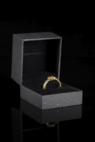 Close-up of a stunning gold and black luxury ring resting on a sleek black velvet cushion with subtle golden glow.