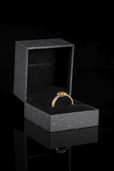 Elegant black velvet jewelry box opened to reveal a shimmering gold ring with subtle diamond accents.