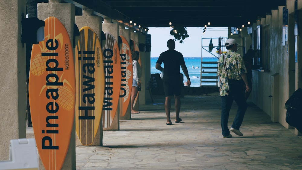 a couple of men walking down a hallway next to surfboards