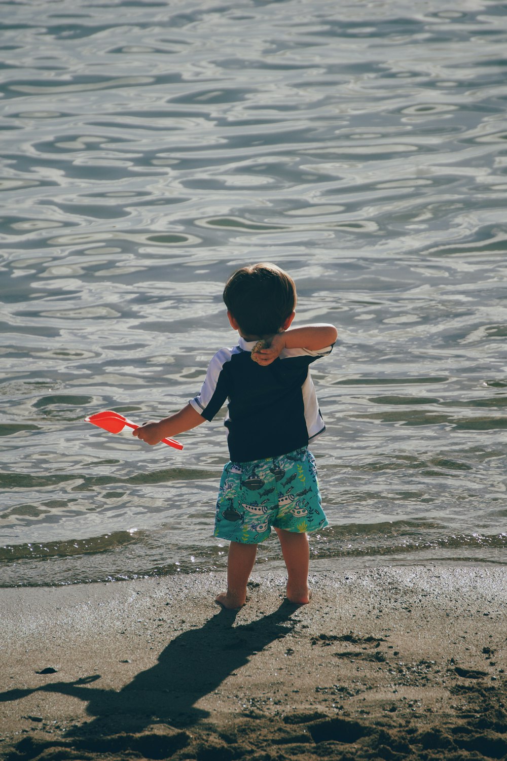 a young boy standing on top of a beach next to a body of water