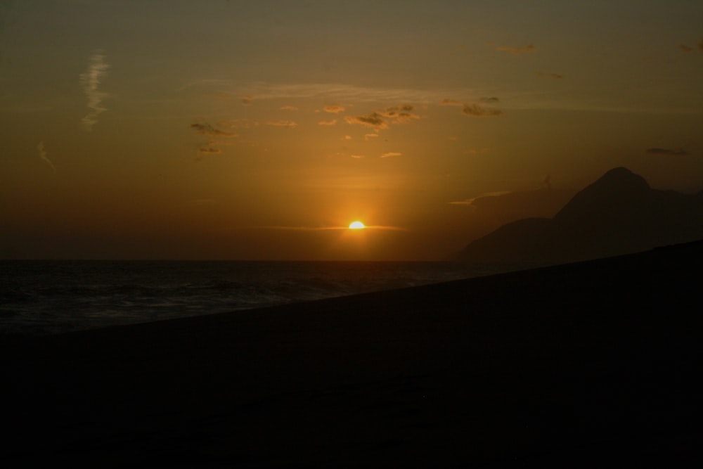 the sun is setting over the ocean with a mountain in the background