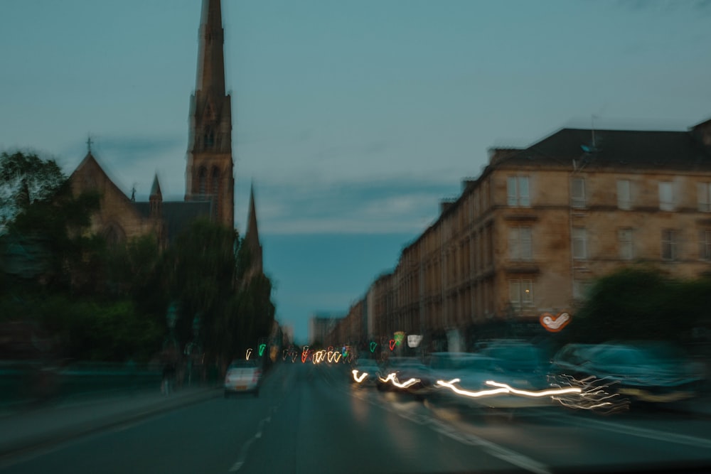 a blurry photo of a city street with a church steeple in the background