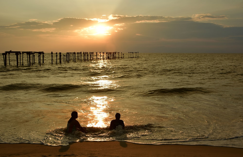 two people are sitting in the water at the beach