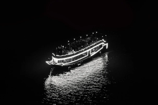 A panoramic view of a boat party with colorful lights reflecting on the water at night.
