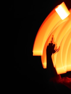 An abstract image featuring a hand in silhouette against a backdrop of vivid, swirling orange light. The light creates a dynamic and energetic pattern on the dark background.