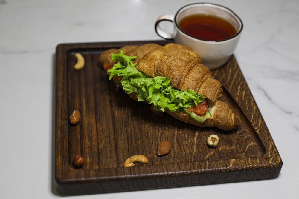 a croissant sandwich with lettuce and a cup of tea