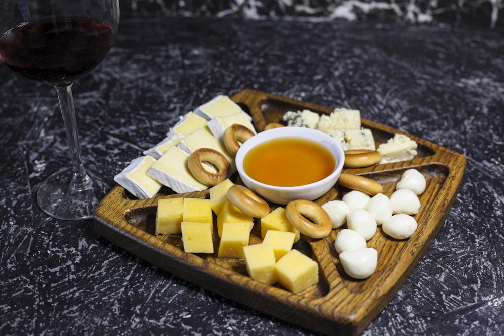 a wooden plate topped with cheese and crackers next to a glass of wine
