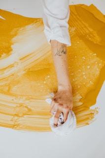 a person with a tattoo on their arm painting a yellow piece of art