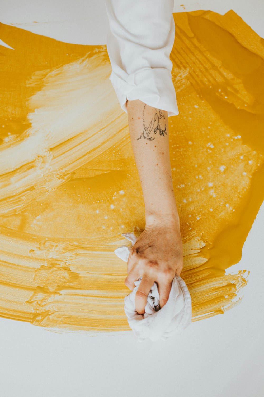 a person with a tattoo on their arm painting a yellow piece of art