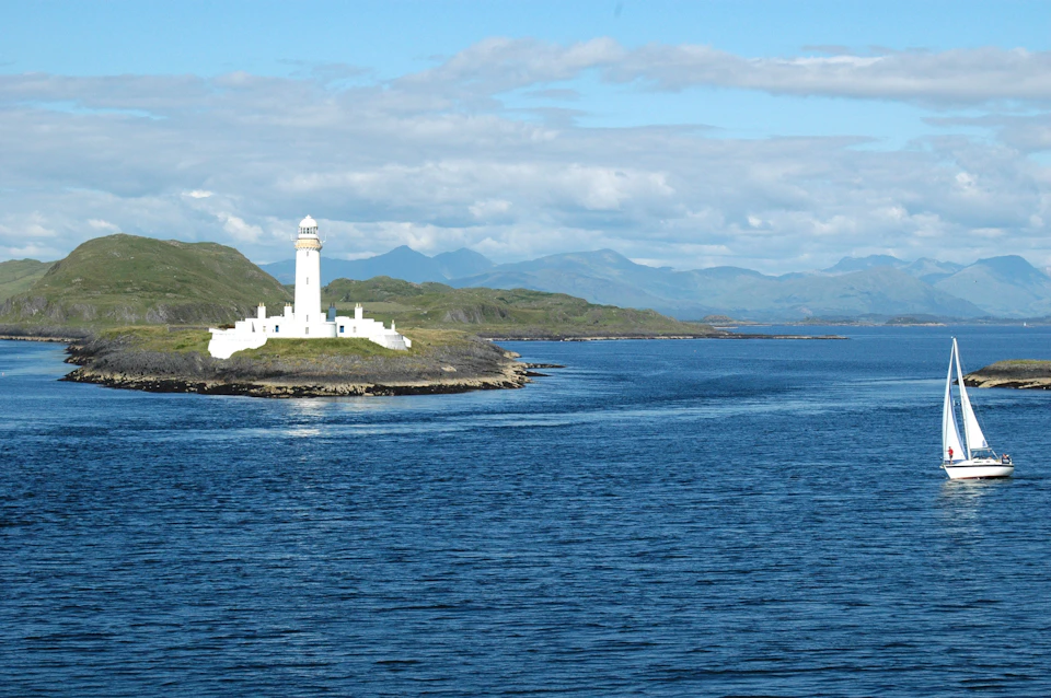 White lighthouse stands tall on island surrounded by mountains and vast ocean waters