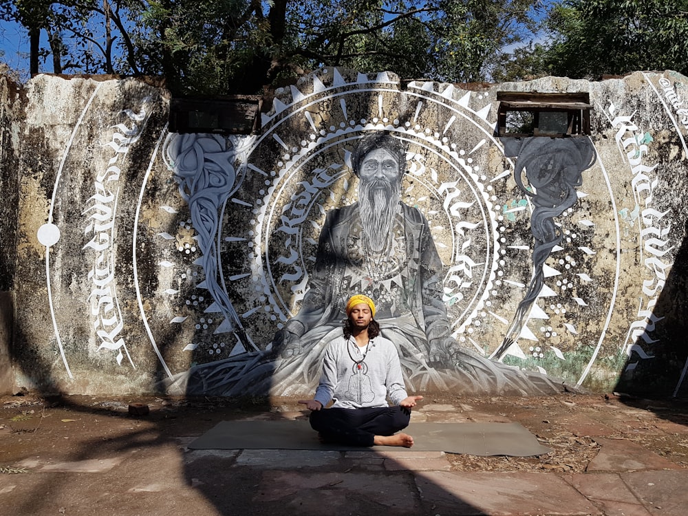 a man sitting on a yoga mat in front of a mural