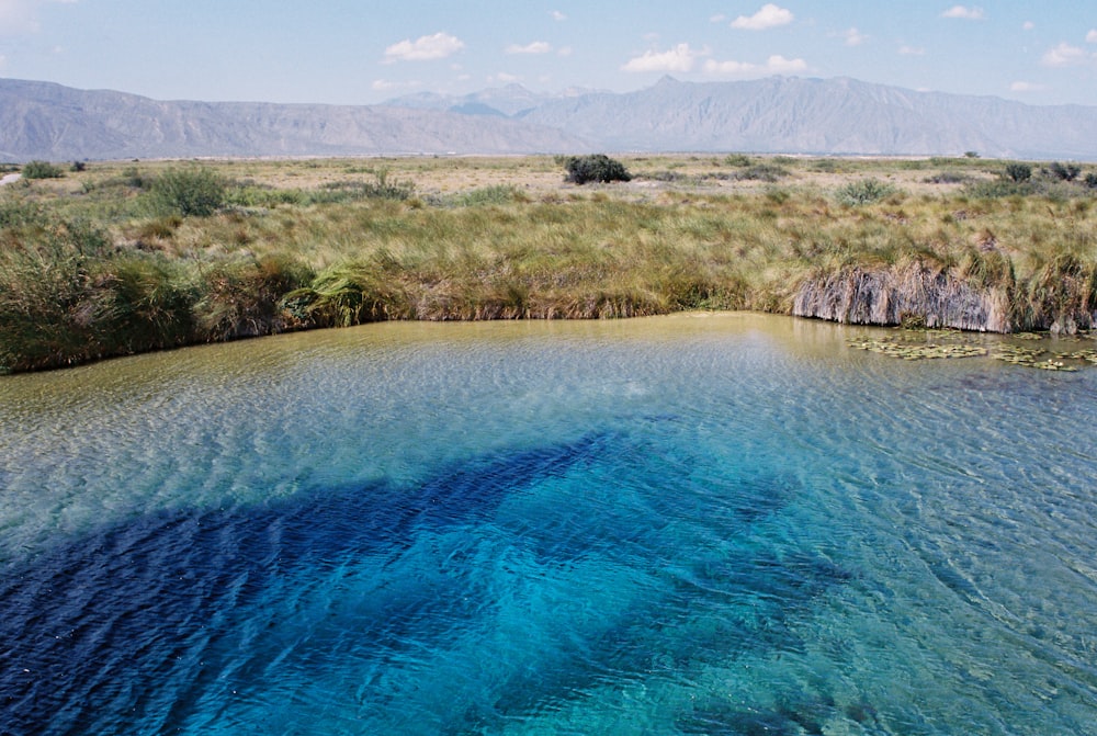 a body of water surrounded by grass and mountains