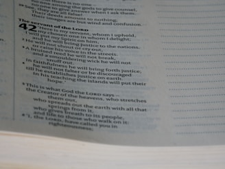A close-up view of a page from a Bible, specifically Isaiah chapter 42. The text discusses themes related to the servant of the Lord. The page's text is in two columns, with a clear serif font.