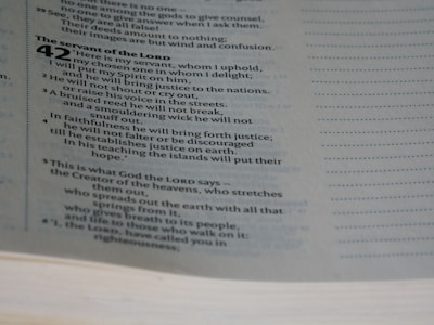 A close-up view of a page from a Bible, specifically Isaiah chapter 42. The text discusses themes related to the servant of the Lord. The page's text is in two columns, with a clear serif font.