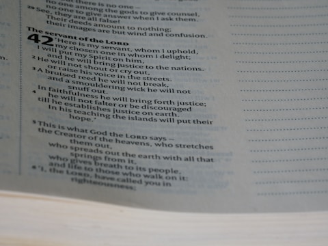 A close-up view of a page from a Bible, specifically Isaiah chapter 42. The text discusses themes related to the servant of the Lord. The page's text is in two columns, with a clear serif font.