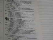 A close-up of an open book page containing text in a column format. The text includes chapter and verse numbers, suggesting a scriptural or biblical passage. The text is organized with some bold headings and varying indentation levels.
