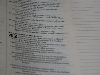 A close-up of an open book page containing text in a column format. The text includes chapter and verse numbers, suggesting a scriptural or biblical passage. The text is organized with some bold headings and varying indentation levels.