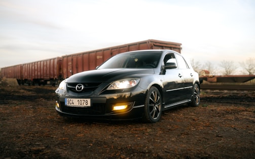 A sleek black VTC car parked beside a train station in a small town.