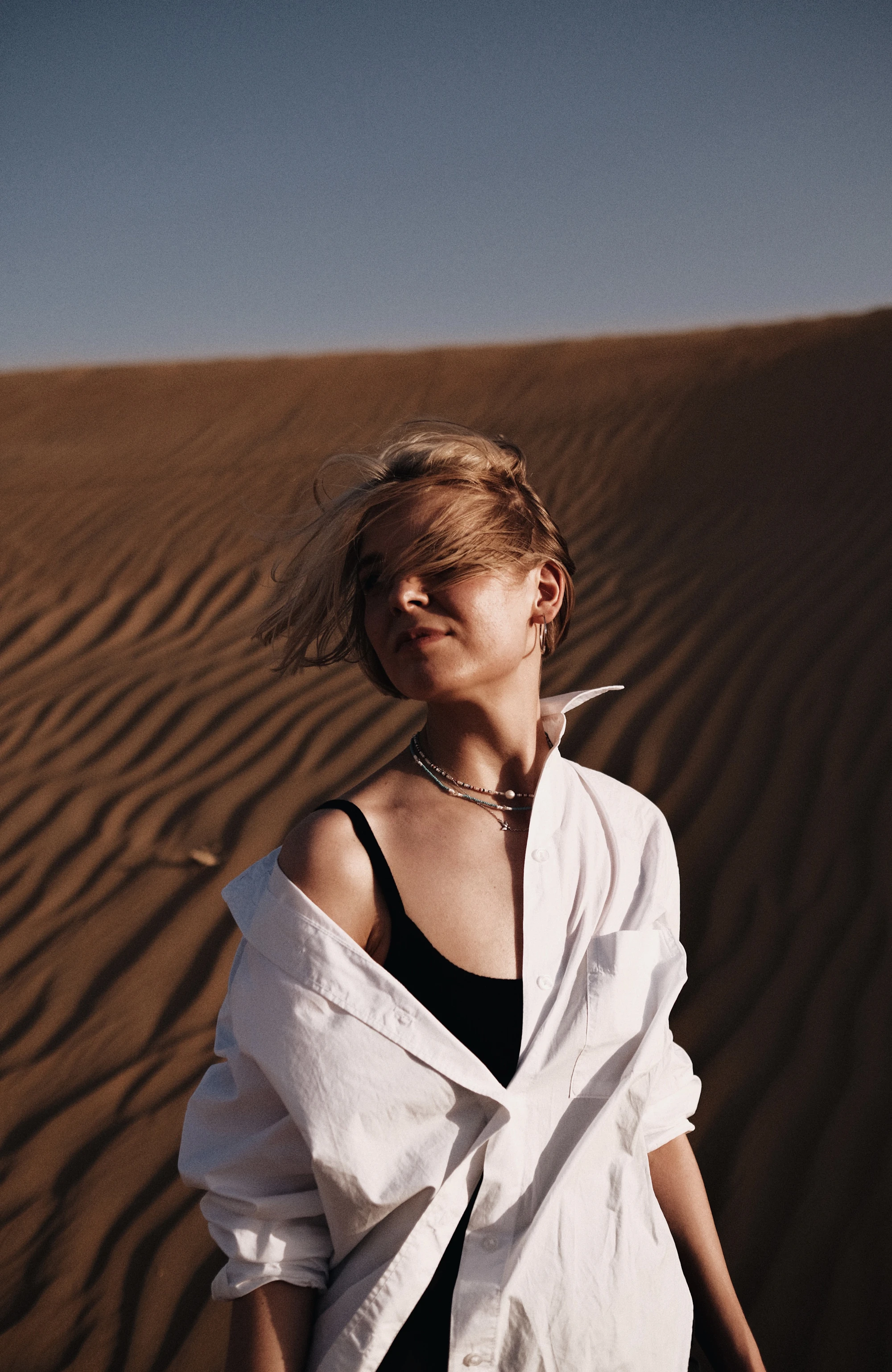 Model in an oversized white shirt standing among desert dunes