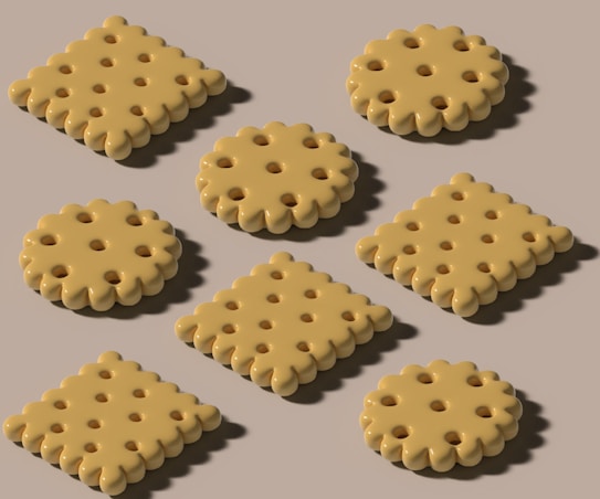 Several biscuits with a perforated pattern are arranged on a plain background. The biscuits are displayed in both round and square shapes, each having a series of evenly spaced holes and a scalloped edge.