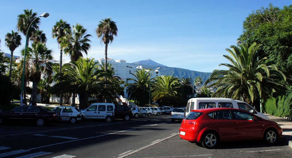 Un coche rojo aparcado en un aparcamiento junto a palmeras