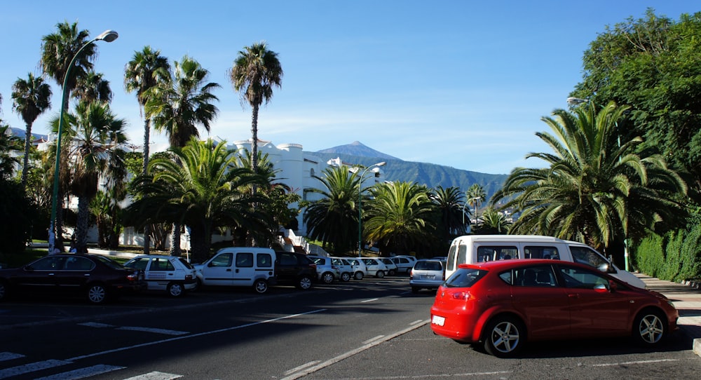 a red car parked in a parking lot next to palm trees