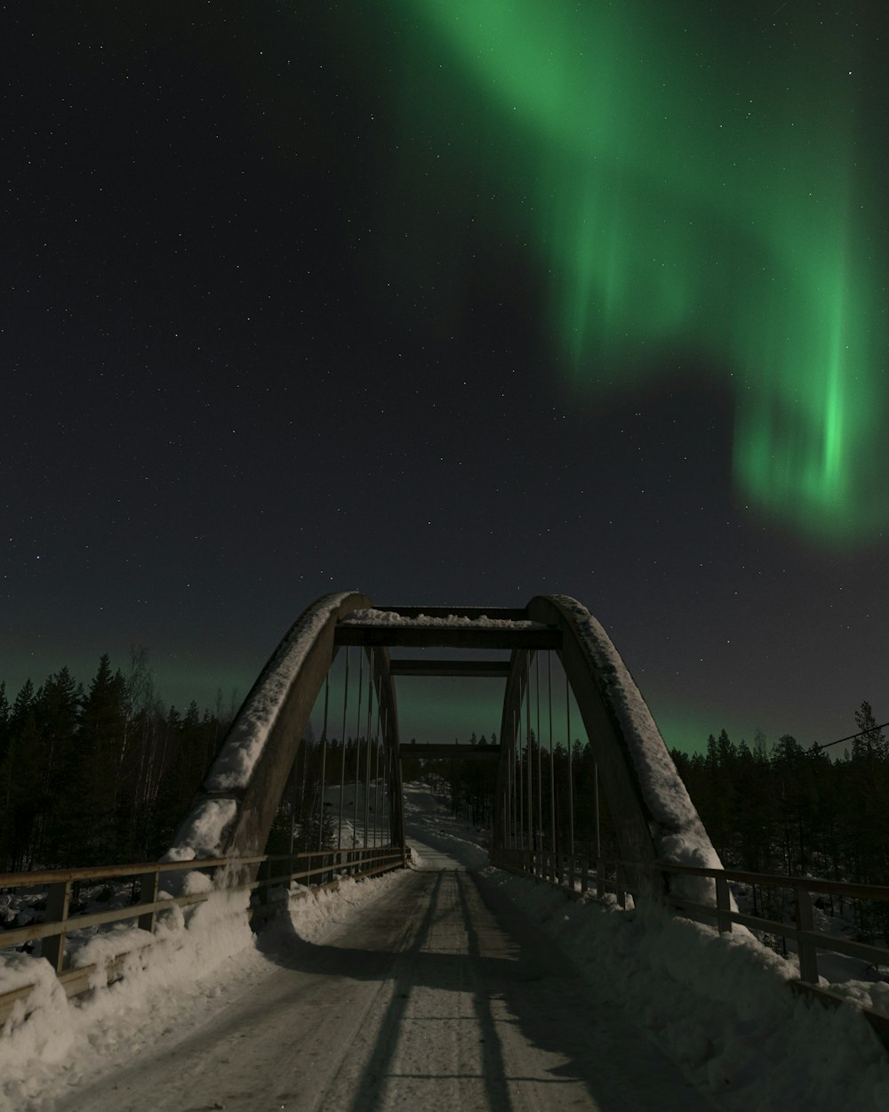 a bridge with snow on the ground and a green light in the sky