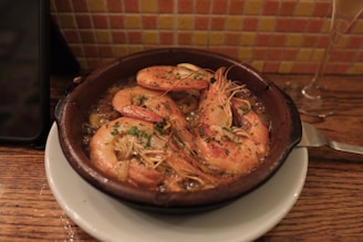 A rustic wooden table with a plate of golden tortillitas de camarones, a glass of sherry wine, and fresh seafood in the background.