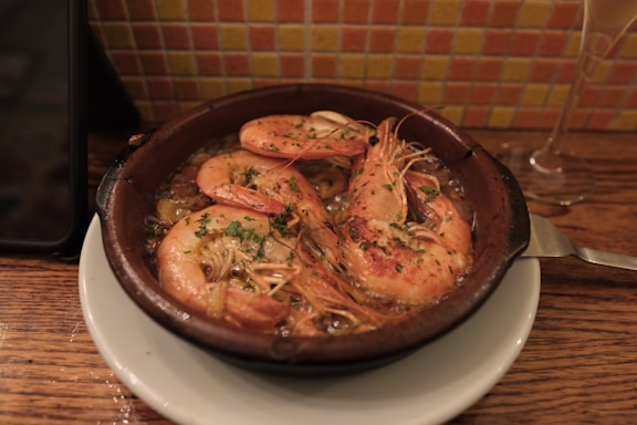 A rustic wooden table with a plate of golden tortillitas de camarones, a glass of sherry wine, and fresh seafood in the background.