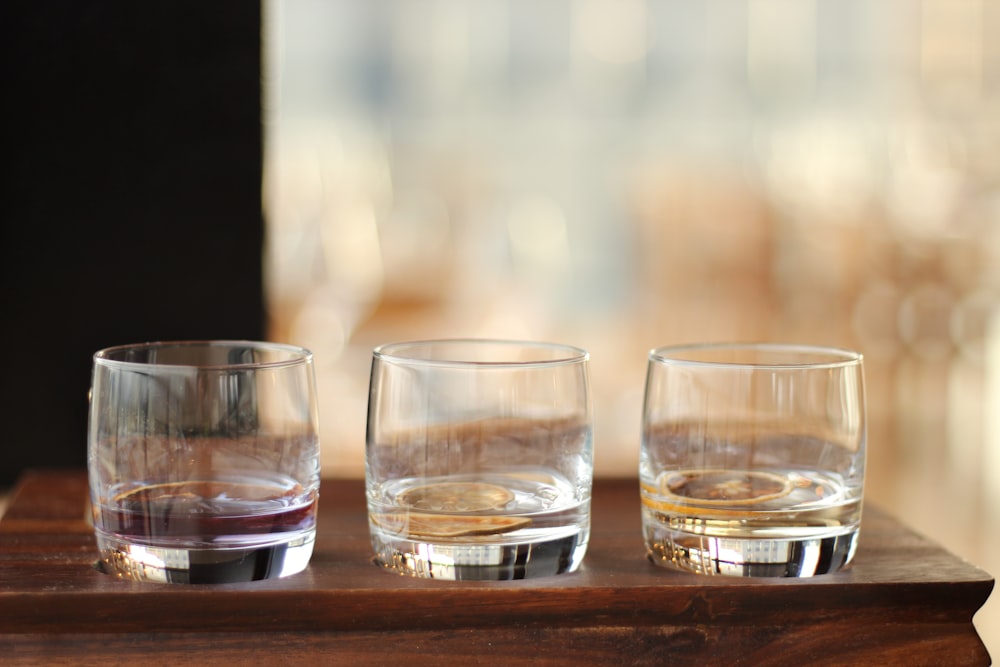 three glasses of alcohol sitting on top of a wooden tray