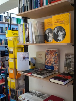 A variety of books are arranged on shelves in a bookstore. Some books are stacked vertically while others are displayed horizontally. Prominent are yellow books with a photo of a woman on the cover. Other books feature different designs and colors. The bookshelves are well-organized, showcasing a diverse collection.