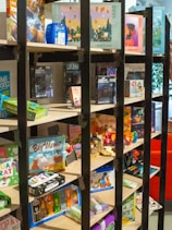 A vibrant display of colorful board games stacked on wooden shelves in a cozy corner.