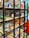 A bookshelf contains a variety of board games, puzzles, and card games. The shelves display colorful and diverse game boxes, with some dedicated to adventure themes. The scene is lively and inviting, with a mix of cartoonish and realistic illustrations on the packaging.