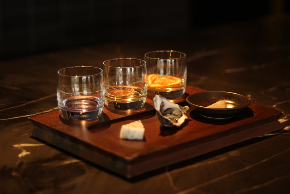 a wooden tray topped with glasses filled with liquid