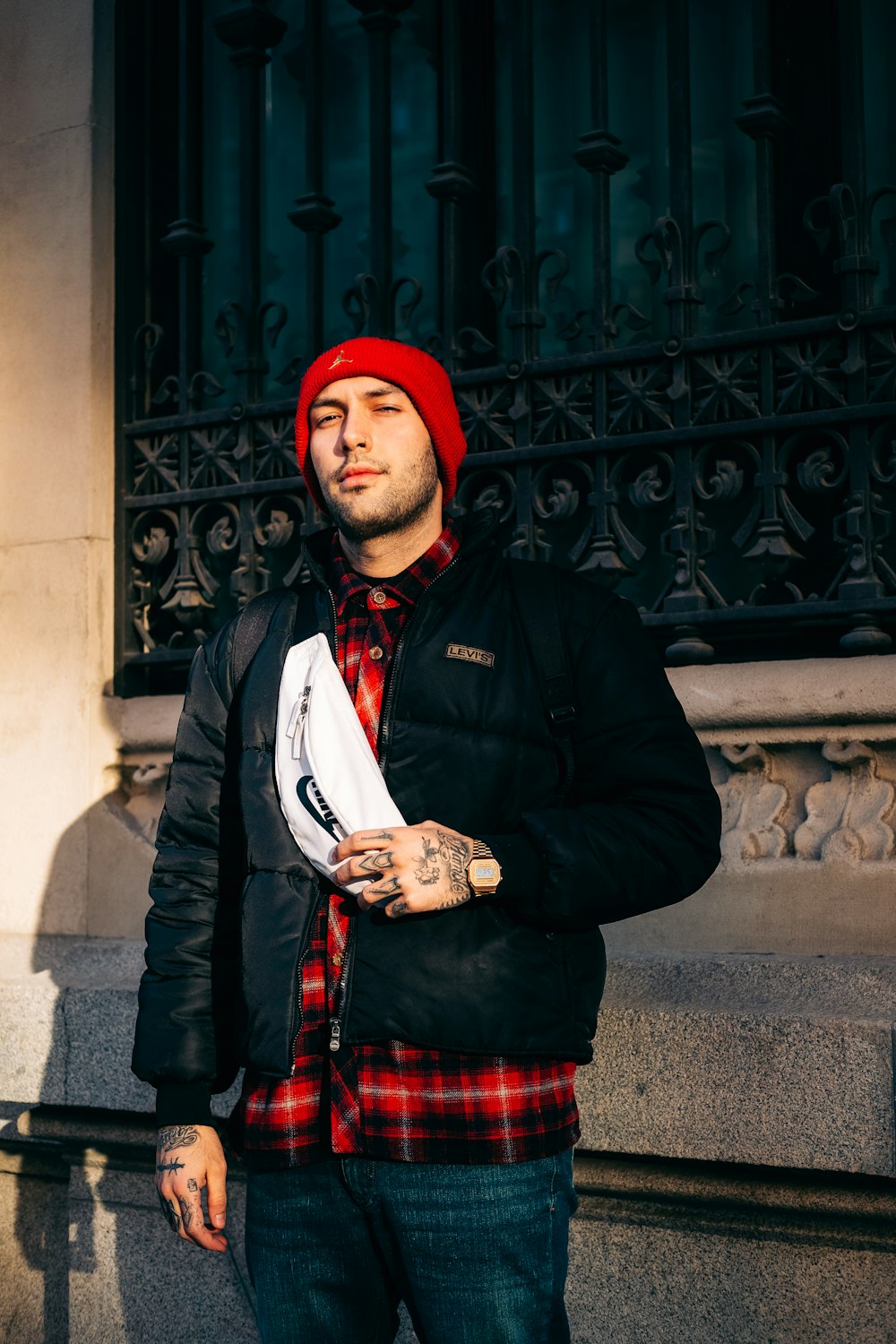 a man standing in front of a building wearing a red hat