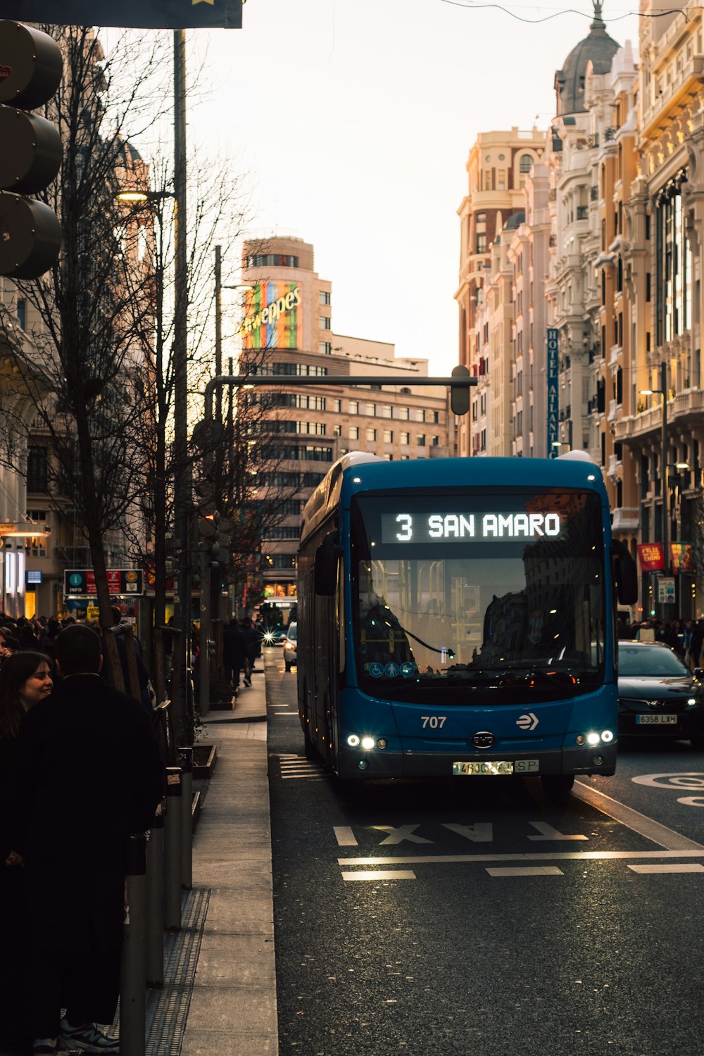 a blue bus driving down a street next to tall buildings